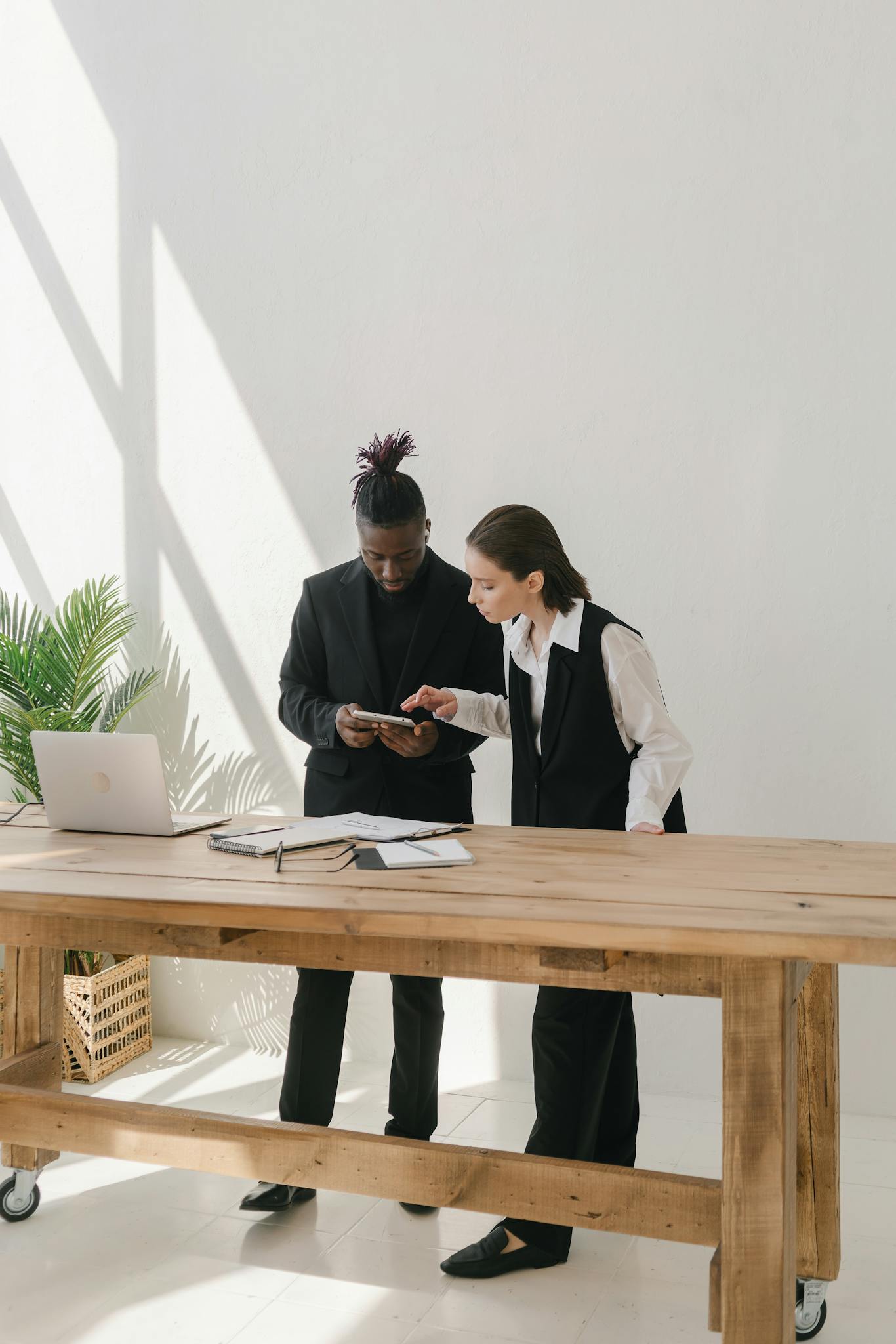 Two business professionals collaborating over a table with documents and a laptop in a bright office.