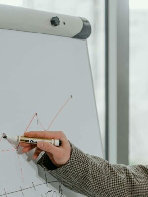 Photo by MART PRODUCTION Close-up of a business professional presenting data with a graph on a whiteboard indoors.